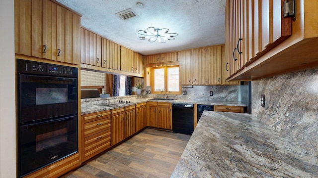 kitchen with black appliances, a sink, light stone counters, a textured ceiling, and wood finished floors