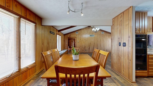 dining room with wood walls, a textured ceiling, lofted ceiling with beams, and wood finished floors