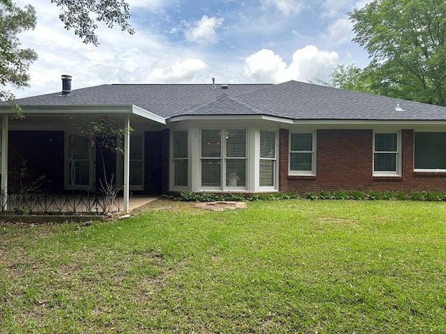 back of property featuring a lawn, roof with shingles, brick siding, and a patio