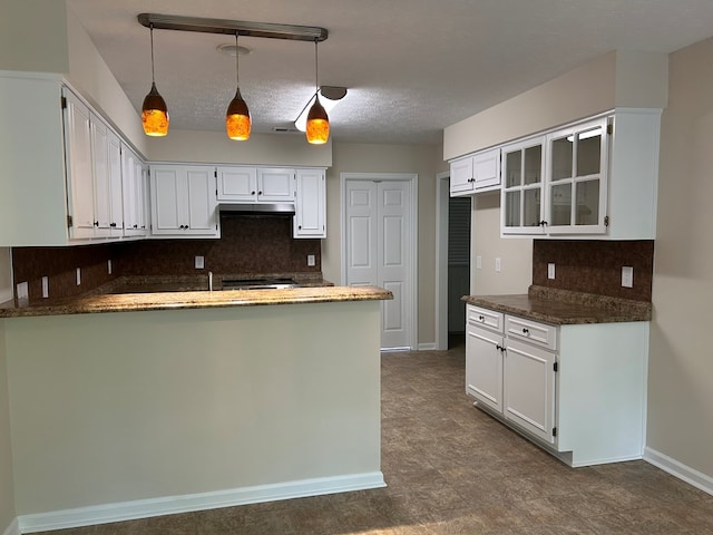 kitchen with white cabinets, a peninsula, baseboards, backsplash, and under cabinet range hood