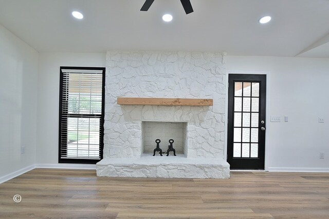 unfurnished living room featuring recessed lighting, a stone fireplace, baseboards, and wood finished floors