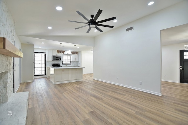 unfurnished living room with light wood finished floors, visible vents, lofted ceiling, a fireplace, and a sink