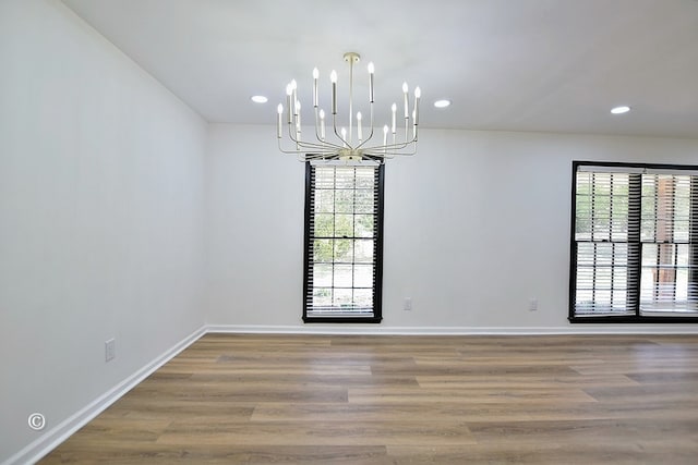 unfurnished dining area with an inviting chandelier, baseboards, wood finished floors, and recessed lighting