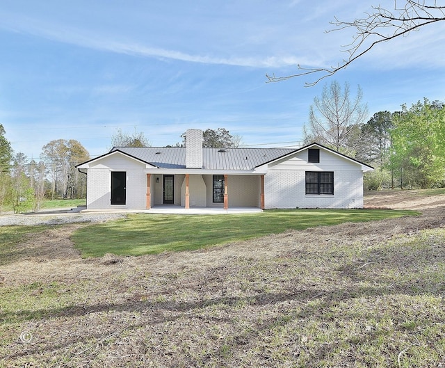 rear view of house with a lawn, a patio, a chimney, metal roof, and brick siding