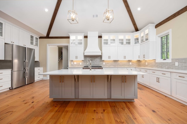 kitchen featuring high end fridge, premium range hood, white cabinetry, and tasteful backsplash