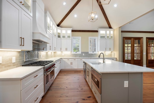 kitchen with white cabinetry, stainless steel appliances, backsplash, a center island with sink, and custom exhaust hood