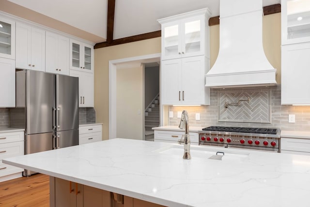 kitchen with white cabinetry, custom range hood, backsplash, and light hardwood / wood-style flooring