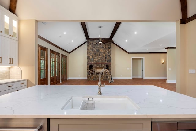 kitchen with white cabinets, lofted ceiling with beams, sink, light hardwood / wood-style floors, and light stone counters