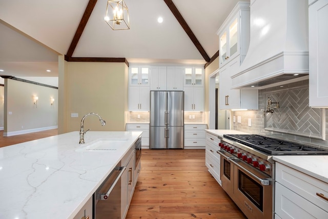 kitchen with white cabinetry, sink, stainless steel appliances, light stone counters, and premium range hood