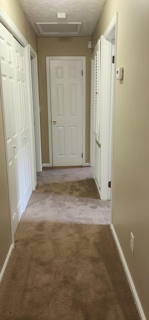 hall with attic access, carpet, baseboards, and a textured ceiling