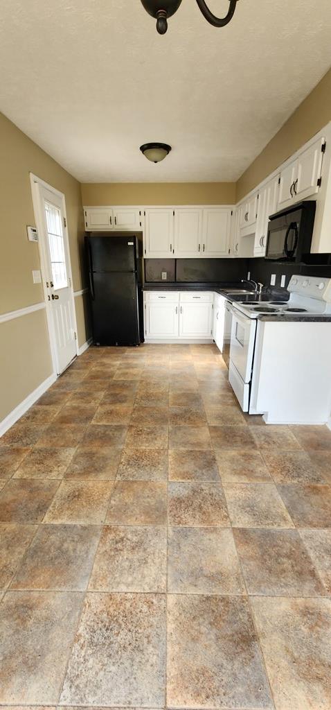 kitchen with black appliances, dark countertops, white cabinets, baseboards, and stone finish flooring