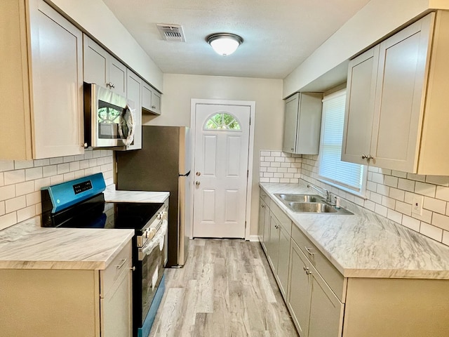 kitchen featuring black electric range, decorative backsplash, light hardwood / wood-style floors, and sink