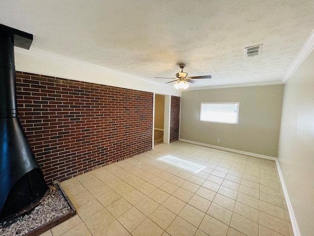 spare room featuring brick wall, ceiling fan, crown molding, light tile patterned floors, and a wood stove