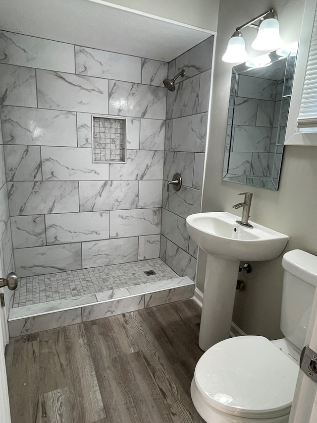 bathroom with a tile shower, hardwood / wood-style floors, and toilet