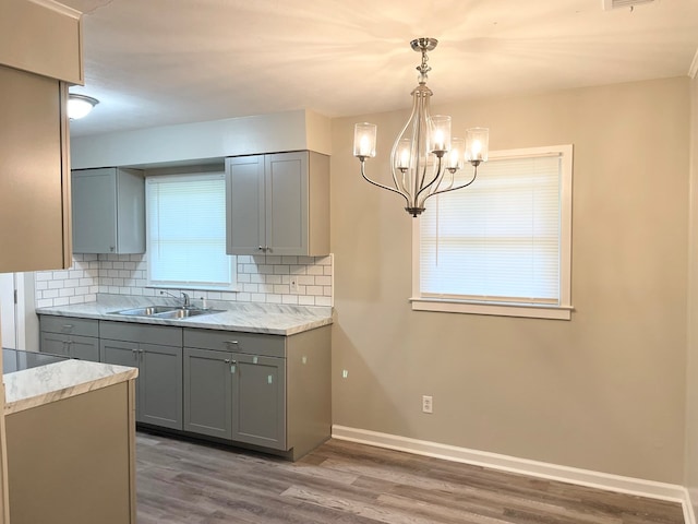 kitchen with decorative backsplash, gray cabinetry, sink, hardwood / wood-style flooring, and hanging light fixtures