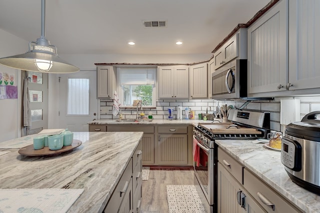 kitchen featuring light stone counters, hanging light fixtures, gray cabinets, and appliances with stainless steel finishes