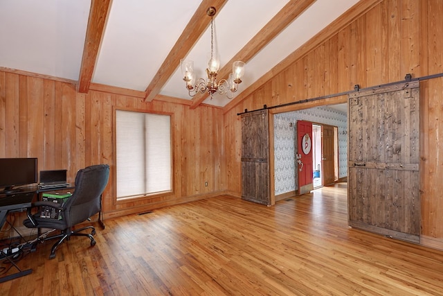 office space featuring wood walls, an inviting chandelier, lofted ceiling with beams, light wood-type flooring, and a barn door