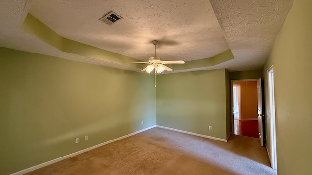 spare room with light carpet, ceiling fan, a tray ceiling, and a textured ceiling