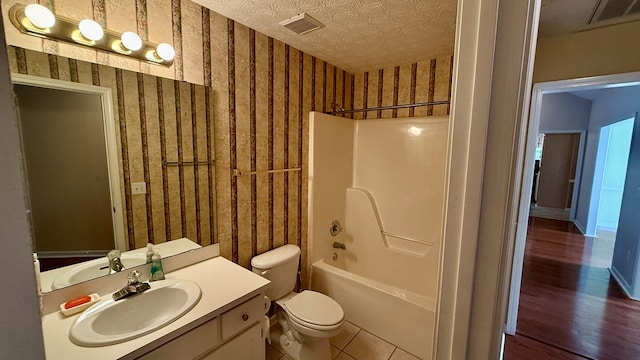 full bathroom with tile patterned flooring, vanity,  shower combination, toilet, and a textured ceiling