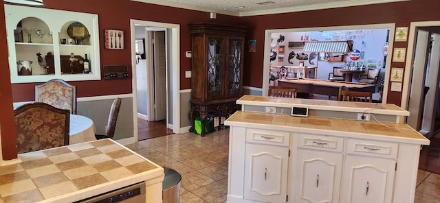 kitchen featuring white cabinetry, light tile patterned flooring, a textured ceiling, and ornamental molding