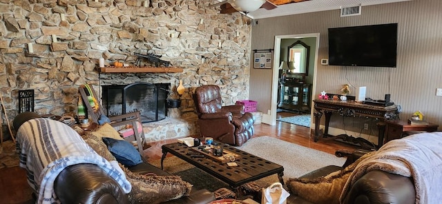 living room featuring wood-type flooring, a stone fireplace, and ceiling fan