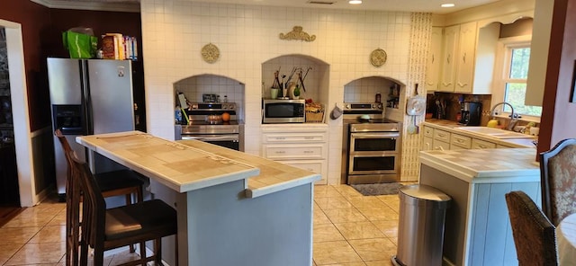 kitchen featuring a kitchen bar, appliances with stainless steel finishes, decorative backsplash, sink, and light tile patterned floors