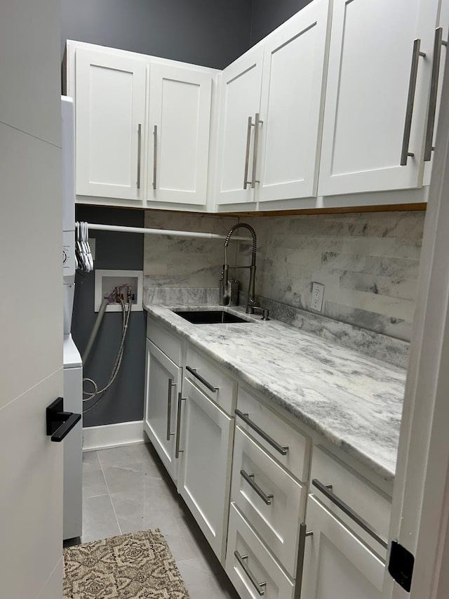 interior space with tasteful backsplash, white cabinetry, a sink, and light stone counters