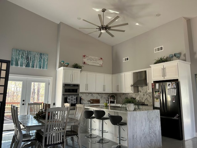 kitchen featuring visible vents, double oven, wall chimney range hood, and freestanding refrigerator