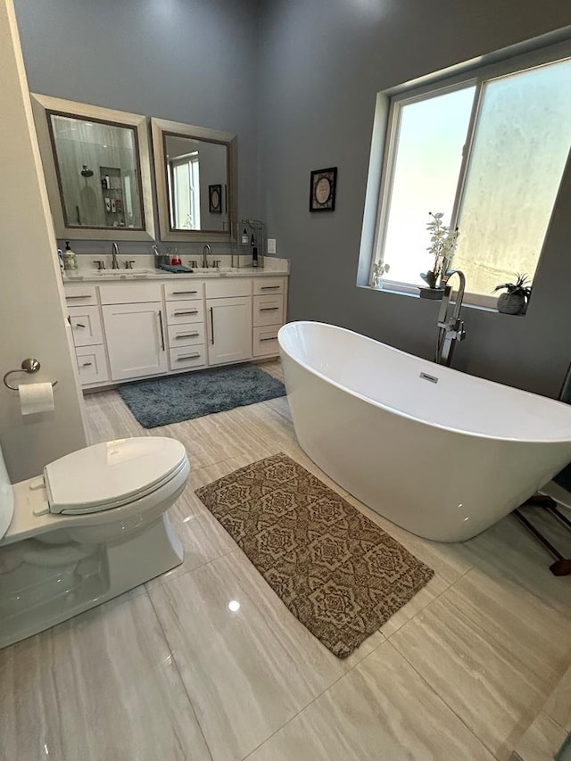 bathroom with a freestanding bath, double vanity, a sink, and toilet