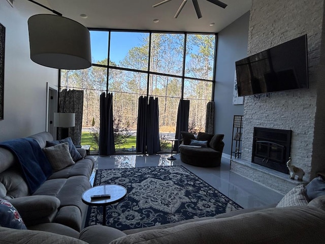 living room featuring expansive windows, ceiling fan, a stone fireplace, and a towering ceiling