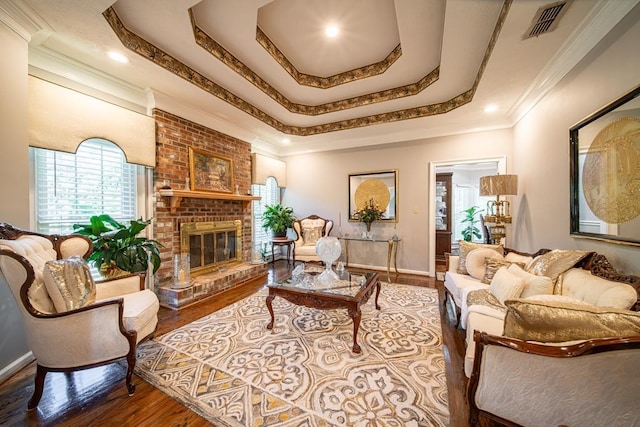 living room featuring a raised ceiling, a fireplace, wood-type flooring, and ornamental molding