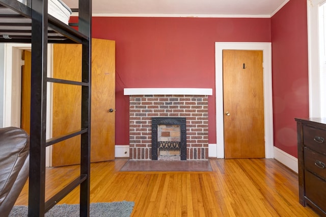 bedroom featuring ornamental molding, a brick fireplace, baseboards, and wood finished floors