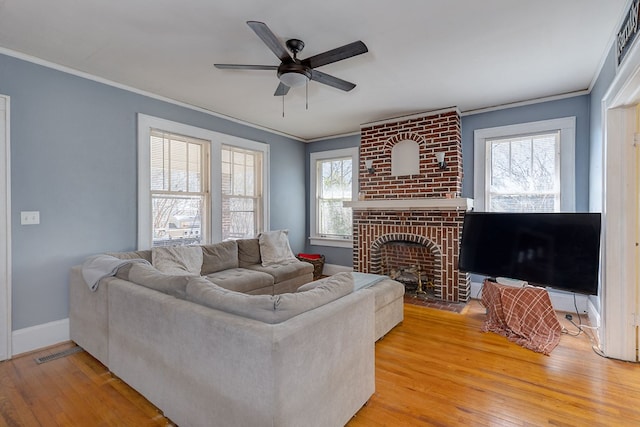 living room with baseboards, ceiling fan, ornamental molding, light wood-style floors, and a fireplace