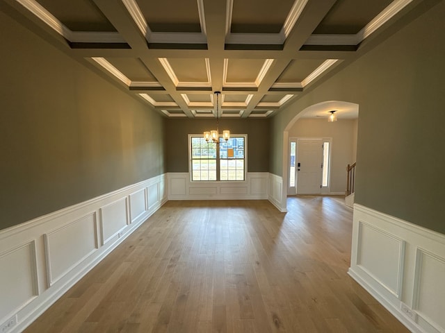 spare room with light wood-type flooring, ornamental molding, coffered ceiling, a notable chandelier, and beamed ceiling