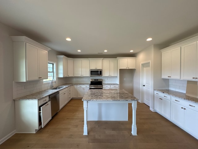 kitchen with white cabinetry, a kitchen island, stainless steel appliances, and light stone counters