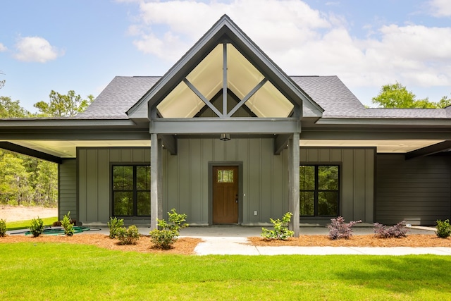 doorway to property with board and batten siding, a shingled roof, and a yard