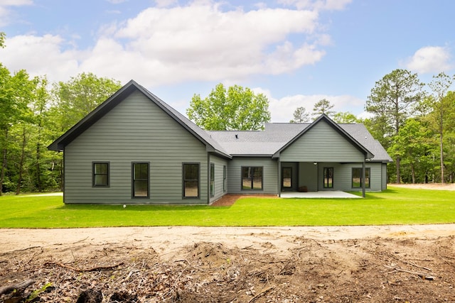 back of property with a patio area, a yard, and roof with shingles