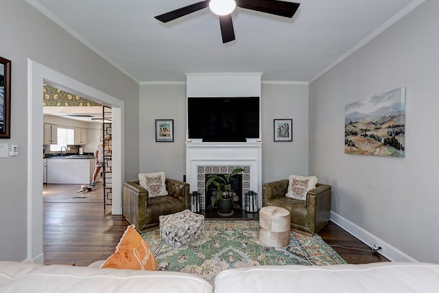 living area with a fireplace, wood finished floors, a ceiling fan, and ornamental molding
