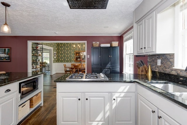 kitchen featuring a peninsula, a healthy amount of sunlight, dark wood-style flooring, white cabinetry, and appliances with stainless steel finishes