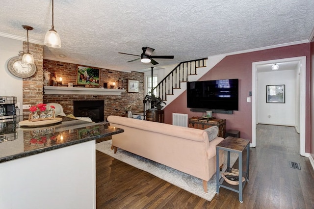 living area with stairway, a ceiling fan, a fireplace, dark wood-type flooring, and visible vents