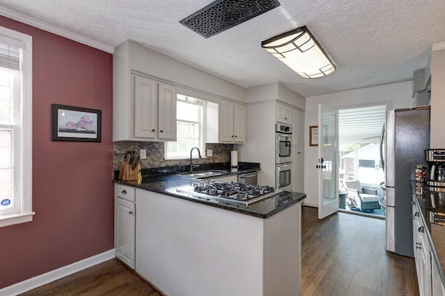 kitchen featuring stainless steel appliances, a sink, dark wood-type flooring, decorative backsplash, and a peninsula
