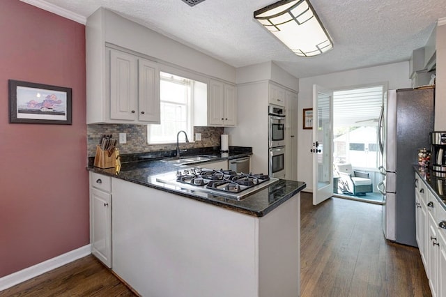kitchen with stainless steel appliances, a peninsula, a sink, dark wood finished floors, and white cabinetry