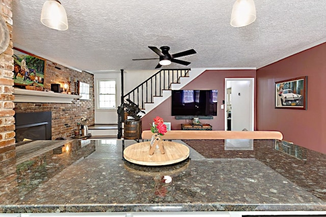 living area with stairs, a textured ceiling, ceiling fan, a fireplace, and ornamental molding
