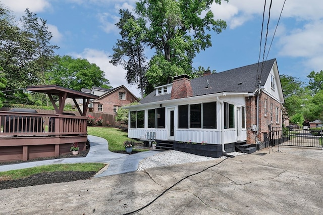 view of front of property featuring a chimney, fence, a wooden deck, entry steps, and a sunroom