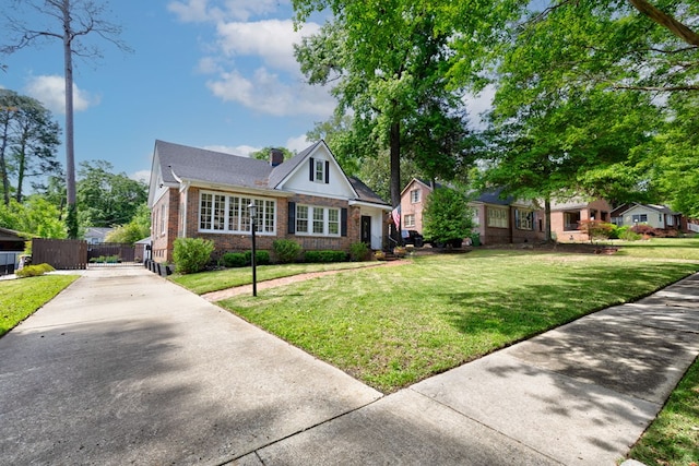 bungalow-style house with a chimney, fence, driveway, brick siding, and a front yard