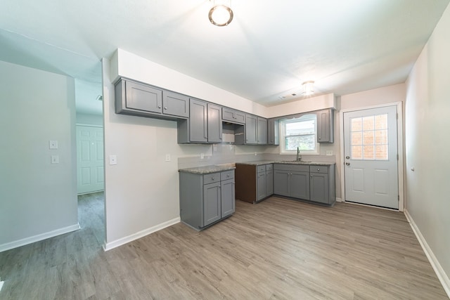 kitchen with stone countertops, light wood-type flooring, gray cabinets, and sink