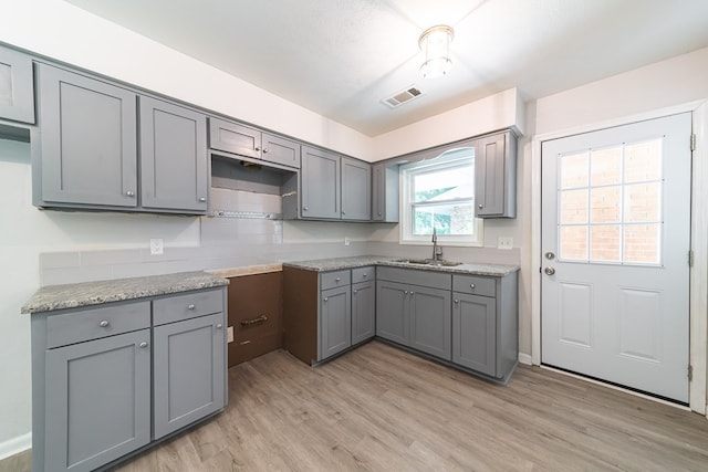 kitchen with light wood-type flooring, light stone counters, gray cabinetry, and sink