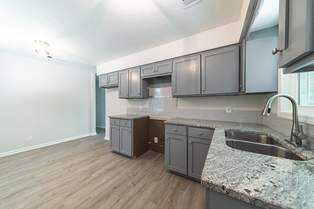 kitchen featuring backsplash, light wood-type flooring, light stone counters, sink, and gray cabinets