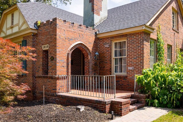view of exterior entry featuring a chimney, brick siding, and a shingled roof