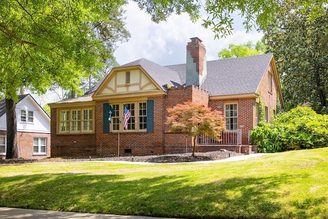 view of front facade with a chimney, a front lawn, roof with shingles, crawl space, and brick siding